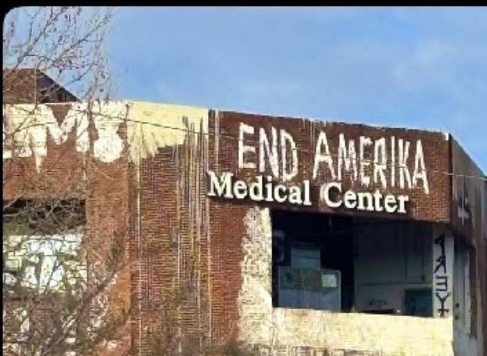 Photo of a brick medical center building painted over with the words "End Amerika".